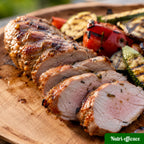 Filet mignon de porc grillé au barbecue, tranché sur planche en bois avec courgettes et poivrons grillés.
