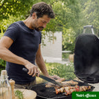 Homme en train de cuire des viandes et brochettes au barbecue dans un jardin, ambiance repas d été.