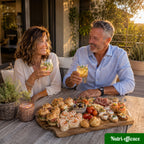 Couple partageant un apéritif convivial sur une terrasse avec cocktails maison, mini burgers, wraps, feuilletés et bouchées apéritives variées