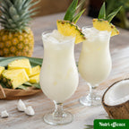 Deux verres de cocktail crémeux ananas coco servis avec glaçons et quartiers d’ananas, dans une ambiance tropicale.