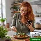 Femme rousse en cuisine tenant un smartphone et dressant un plat maison garni de tomates cerises et salade verte.