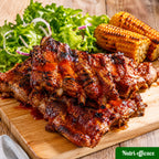 Côtes levées barbecue caramélisées servies sur une planche avec maïs grillé et salade verte.
